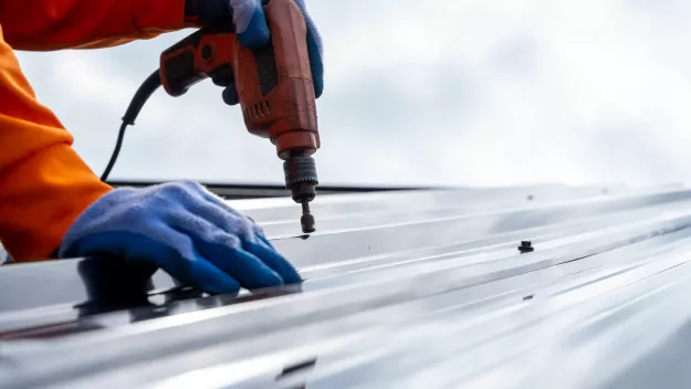 Worker in gloves using a drill on a metal surface.